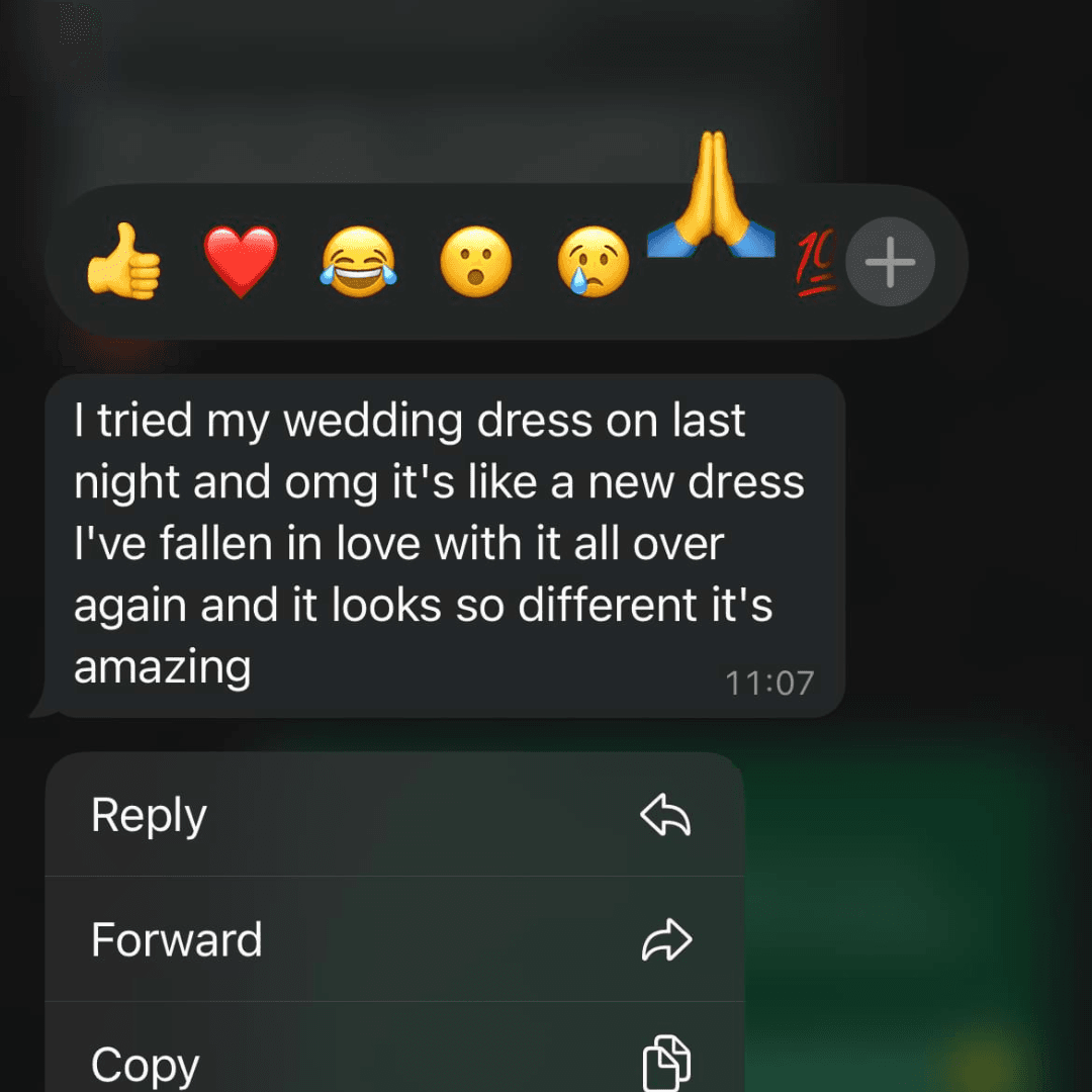 A WhatsApp message at 11:07 with heart, laughing, and prayer emojis. The sender excitedly shares that they tried on their wedding dress again, feeling like it's brand new, and have fallen in love with it all over again.